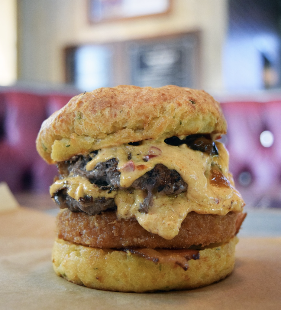 This specialty, limited-time burger features two pressed beef patties, pimento cheese, fried green tomato, bacon, and jalapaño jam between a cheddar-chive biscuit.