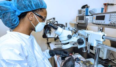student in scrubs working at a microscope with black gloves on