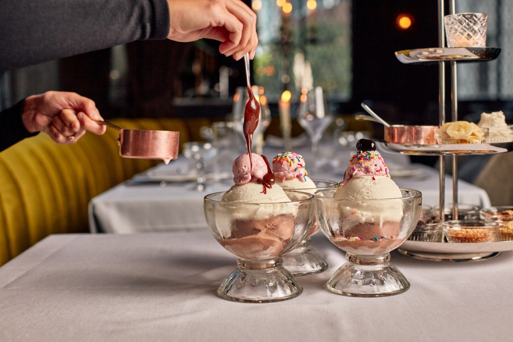 ice cream sundaes on a white table with someone garnishing them