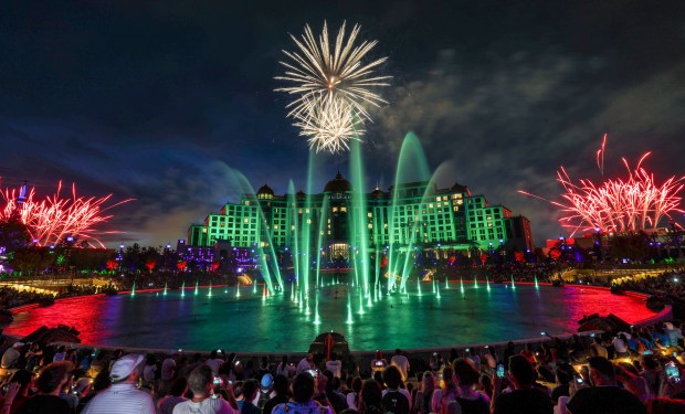 Guests watch the debut of the first nighttime finale fireworks show at Universal Epic Universe in Orlando on Tuesday. With the Helios Grand Hotel as a backdrop, the "Universal Celestial Goodnight" show launches at Cosmos Lagoon and features a highly synchronized production of dancing water fountains and light with music and fireworks. (Joe Burbank/Orlando Sentinel)