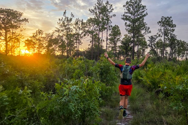 Kevin Bolton throws his hands up in excitement as the sun sets during the Skunk Ape Night Run in Green Swamp on July 18, 2026. (Patrick Connolly/Orlando Sentinel)