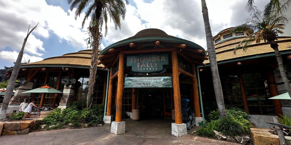 Thunder Falls Terrace entrance at Universal’s Islands of Adventure, framed by palm trees and rustic wood against a partly cloudy sky.