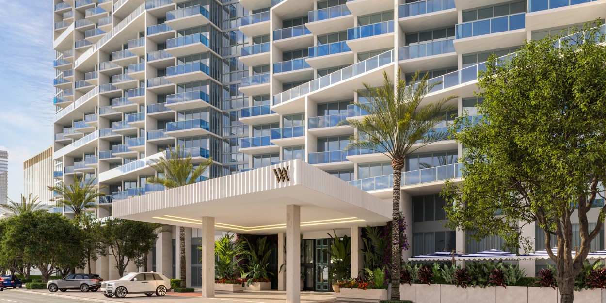 Modern high-rise building with glass balconies and a covered entrance to the Waldorf Astoria Miami Beach surrounded by palm trees and greenery.