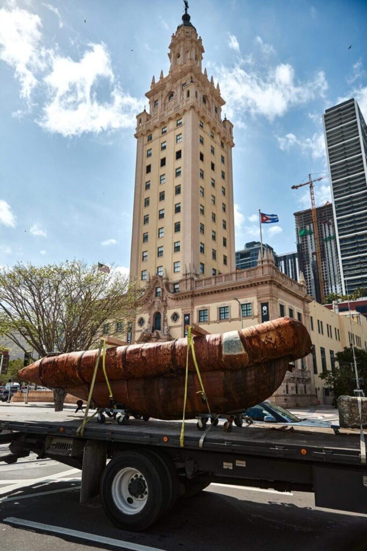 A piece of “Exile” on a flatbed truck on the way to the exhibition passes by the Freedom Tower.
