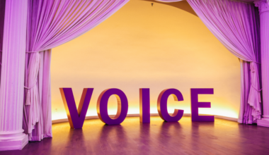 VOICE in big block letters bellow a purple curtain