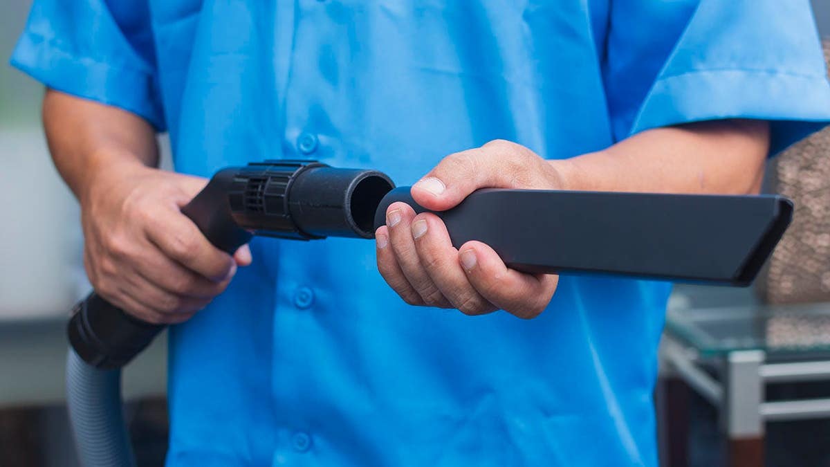 Anonymous person attaching a crevice tool to a vacuum cleaner hose.