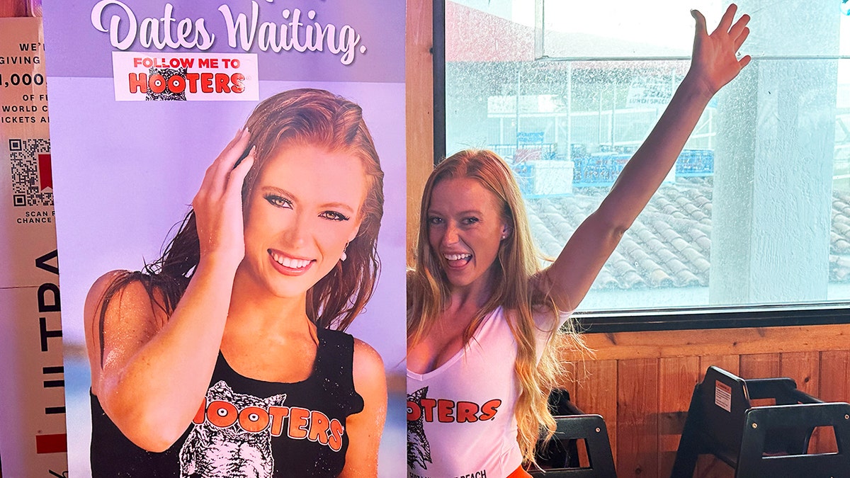 A Hooters girl poses next to an enlarged picture of herself.