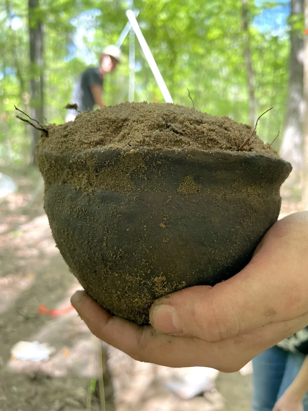 A small clay vessel full of dirt being held in a person's hand