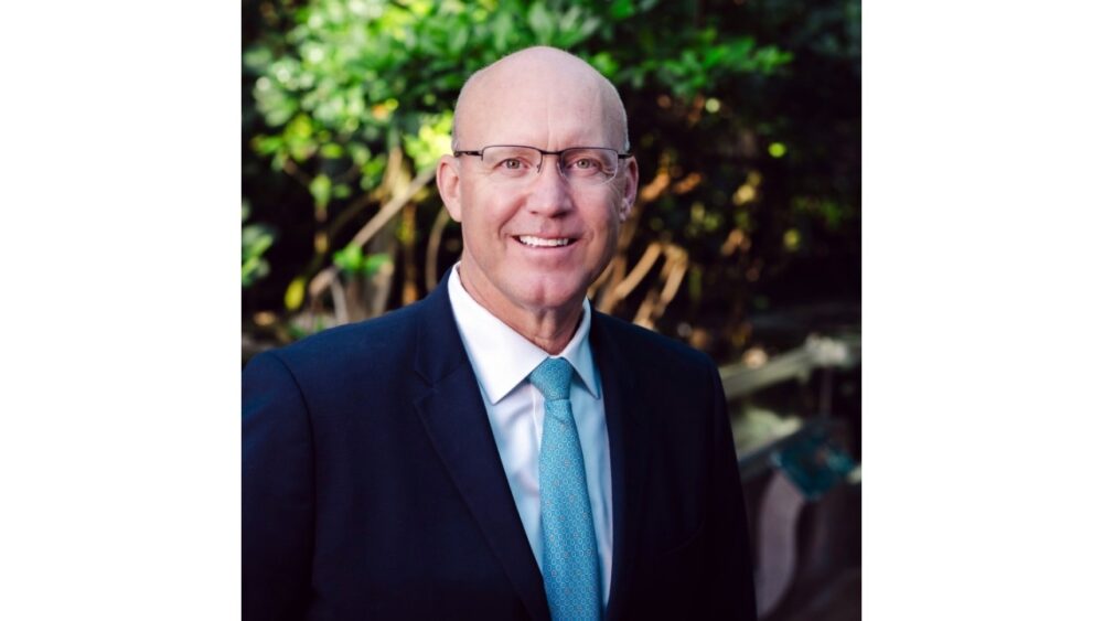 Roger Germann, president and CEO of the Florida Aquarium, poses outdoors in a dark suit and light blue tie.