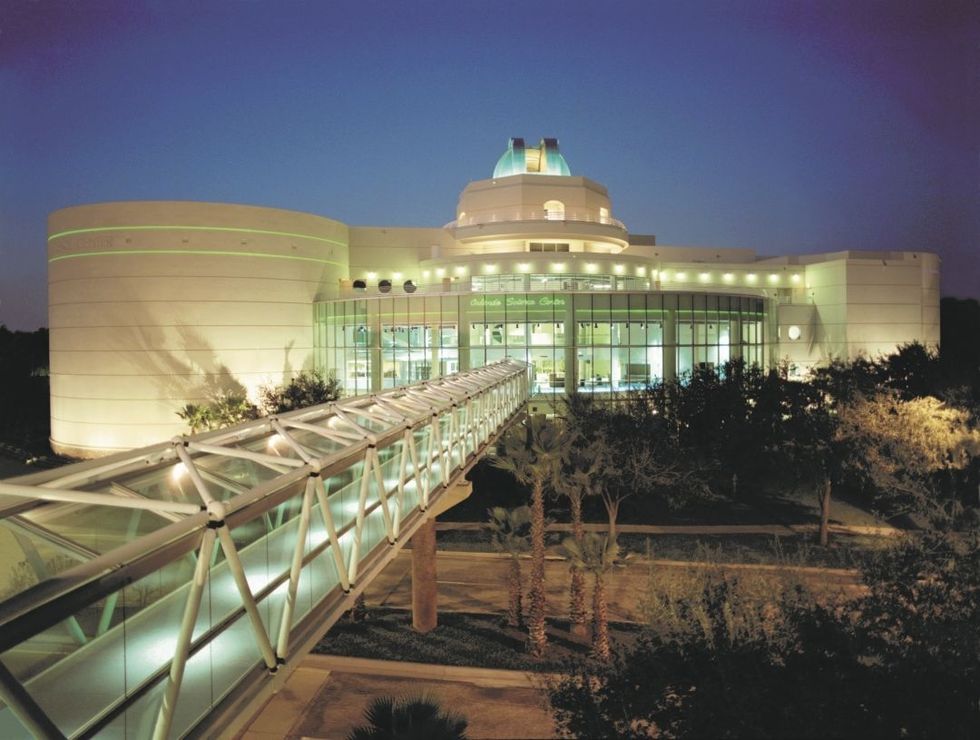 Modern observatory with dome at Orlando Science Centre, illuminated at dusk, connected by a glass bridge.