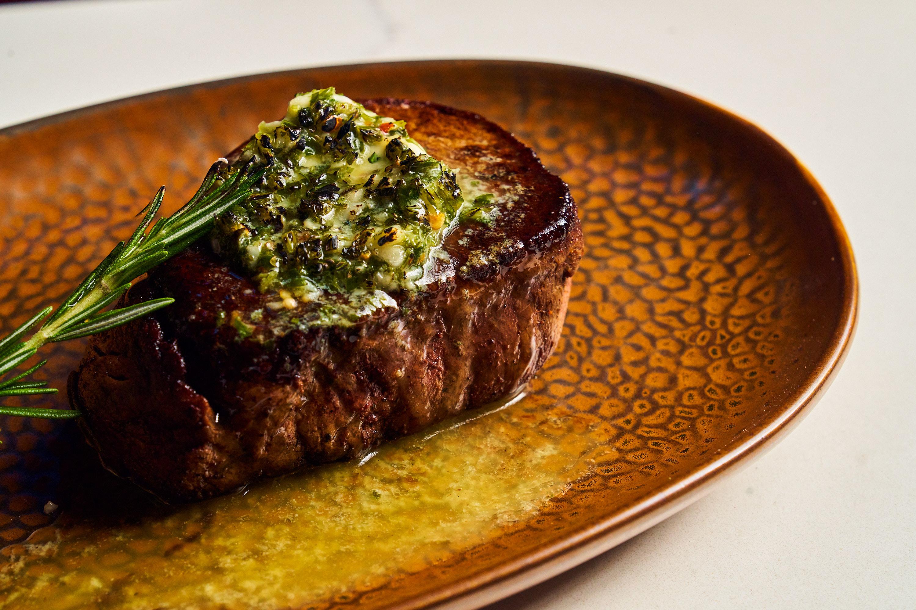 a filet mignon with green sauce on a gold plate