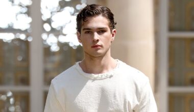 Clavicular in a white outfit walking outdoors, with a neutral expression and styled hair.