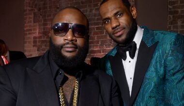 Rick Ross and LeBron James posing together. Rick Ross wears sunglasses and a black suit, LeBron in a teal patterned tuxedo.