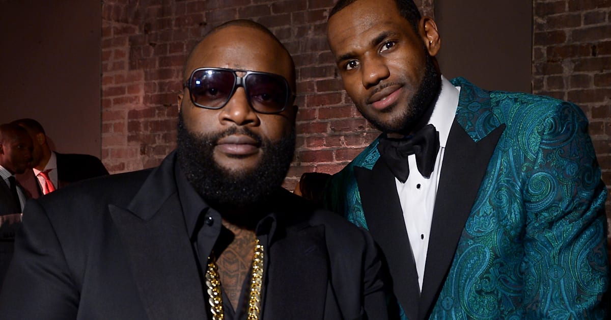 Rick Ross and LeBron James posing together. Rick Ross wears sunglasses and a black suit, LeBron in a teal patterned tuxedo.