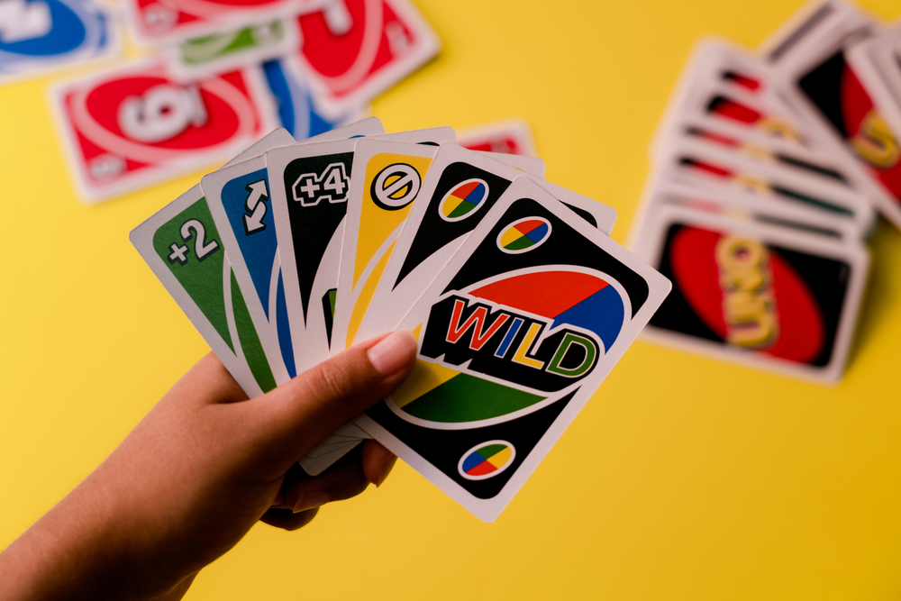 Uno cards held against a deck of cards on a yellow background
