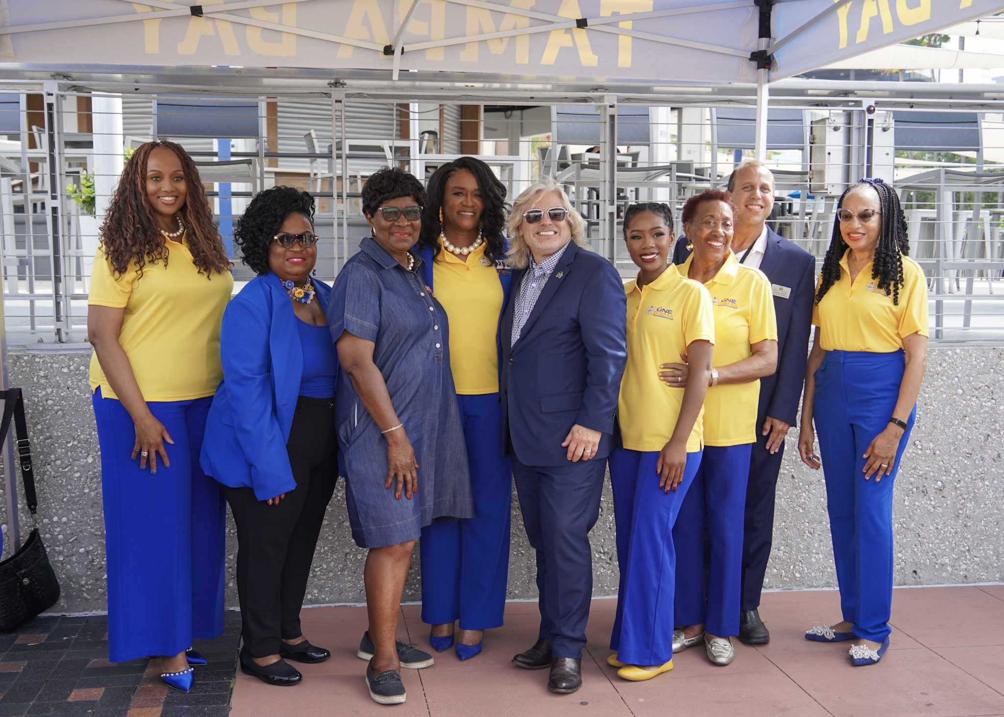 Sigma Gamma Rho leadership and partners pose together under a tent on the Tampa Riverwalk, dressed in vibrant royal blue and yellow attire to celebrate the paver reveal.