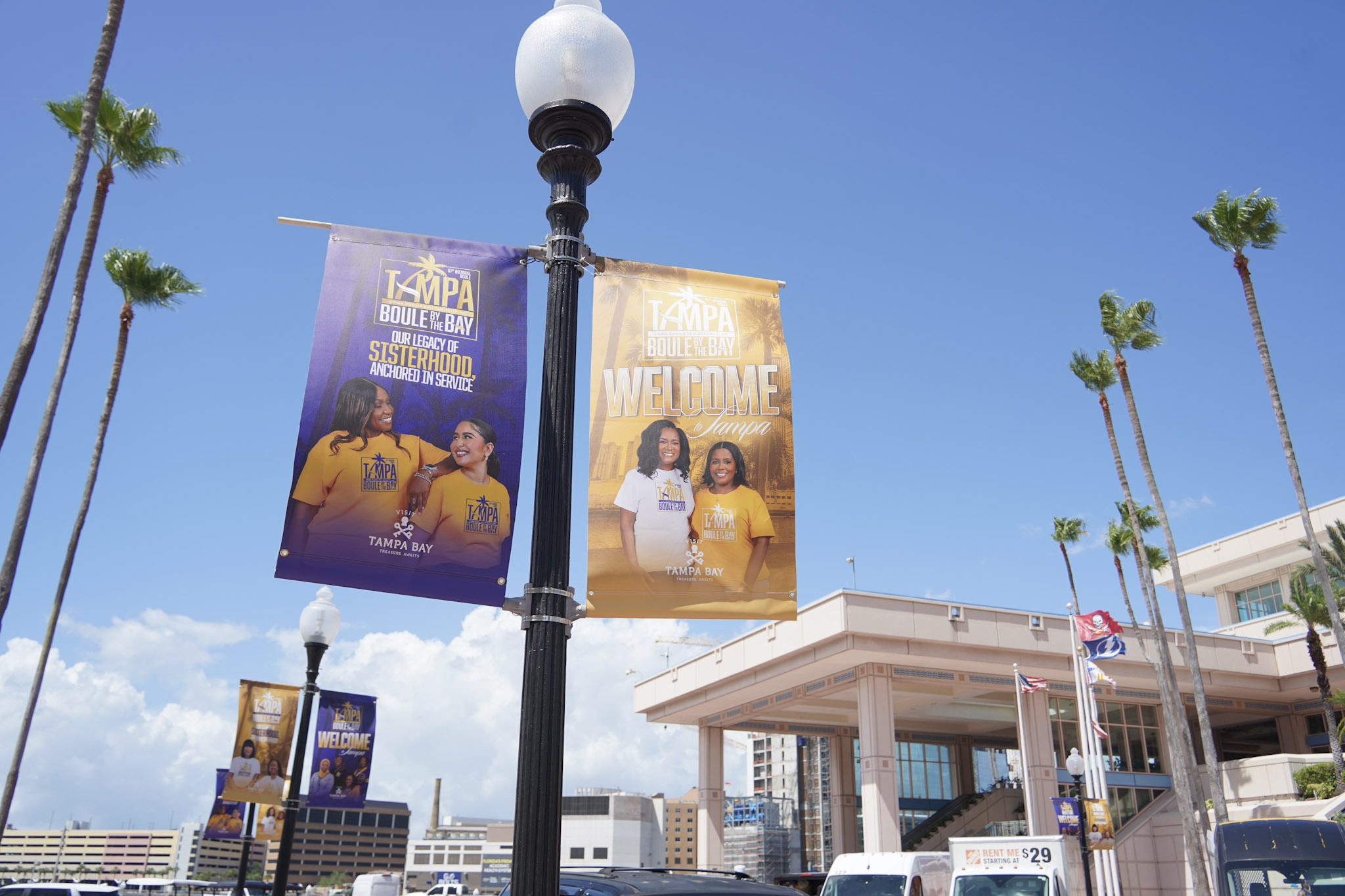 Light pole banners promoting the Sigma Gamma Rho 61st International Biennial Boule with the Tampa Convention Center, palm trees, and blue sky in the background.