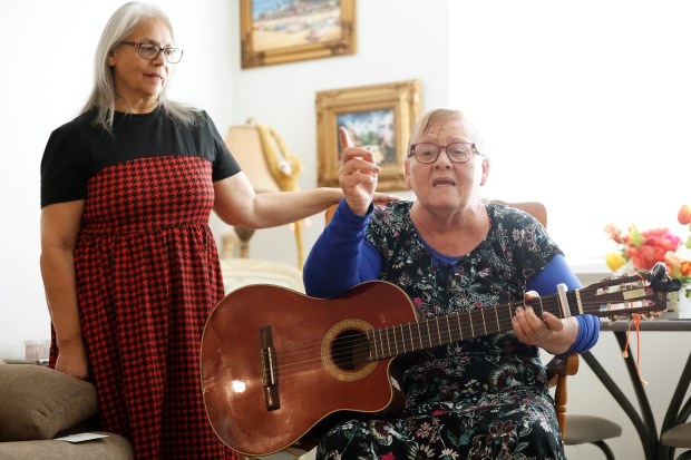Alice Martinez looks on as Julia Santana speaks while holding her guitar in her new apartment in The Enclave at Canopy Park, on Monday, July 13, 2026. Six seniors, who have been living in some pretty horrible conditions due to lack of money, are among the first residents of this new affordable housing complex. (Ricardo Ramirez Buxeda/ Orlando Sentinel)