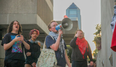 UNF student stand protesting with megaphone, with the Jacksonville skyline in the background.