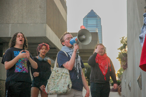UNF student stand protesting with megaphone, with the Jacksonville skyline in the background.