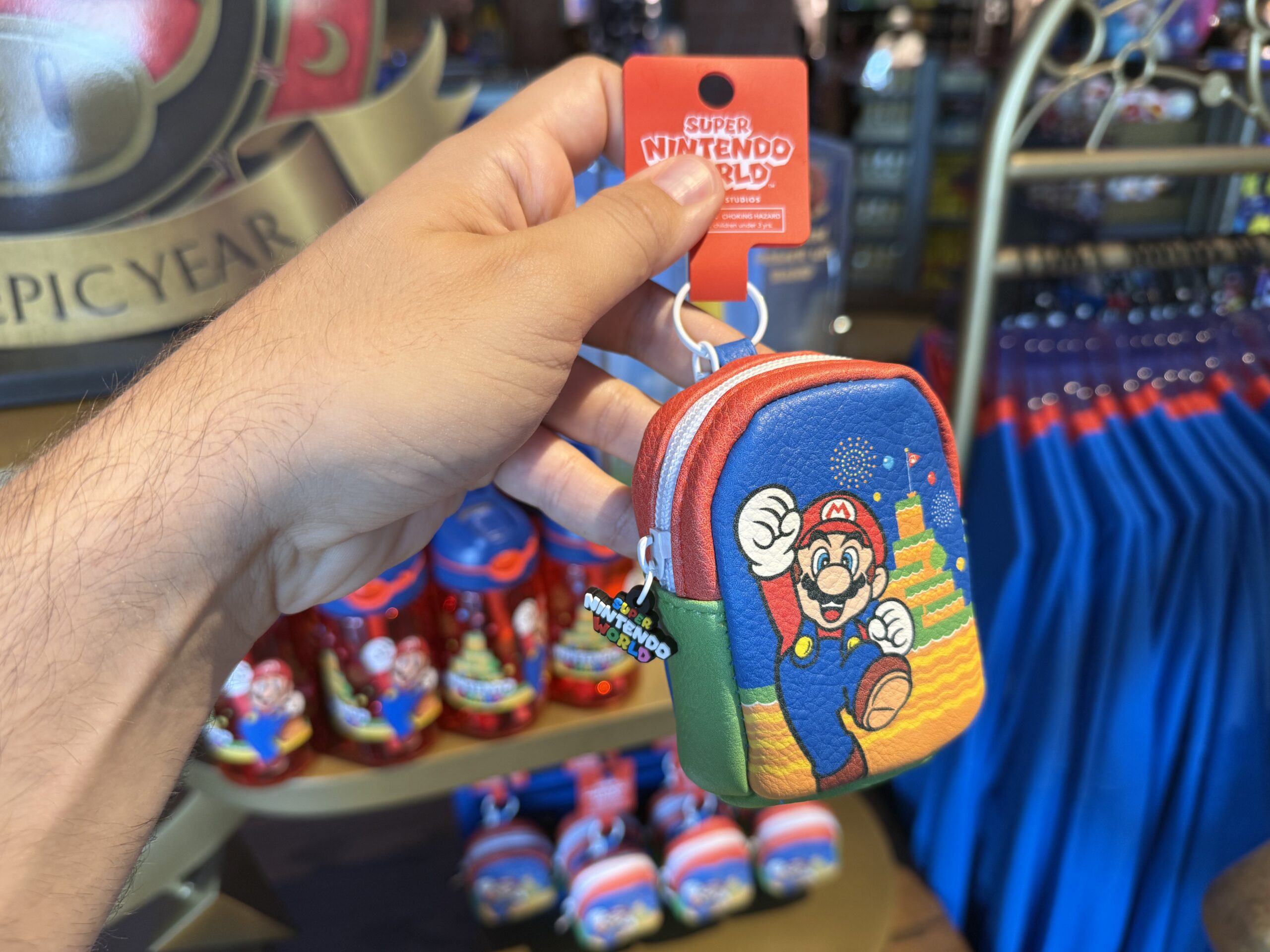This bag charm with Mario and Mount Beanpole can be clipped to a bag and store small items. Attached to the zipper is a charm of the Super Nintendo World logo.