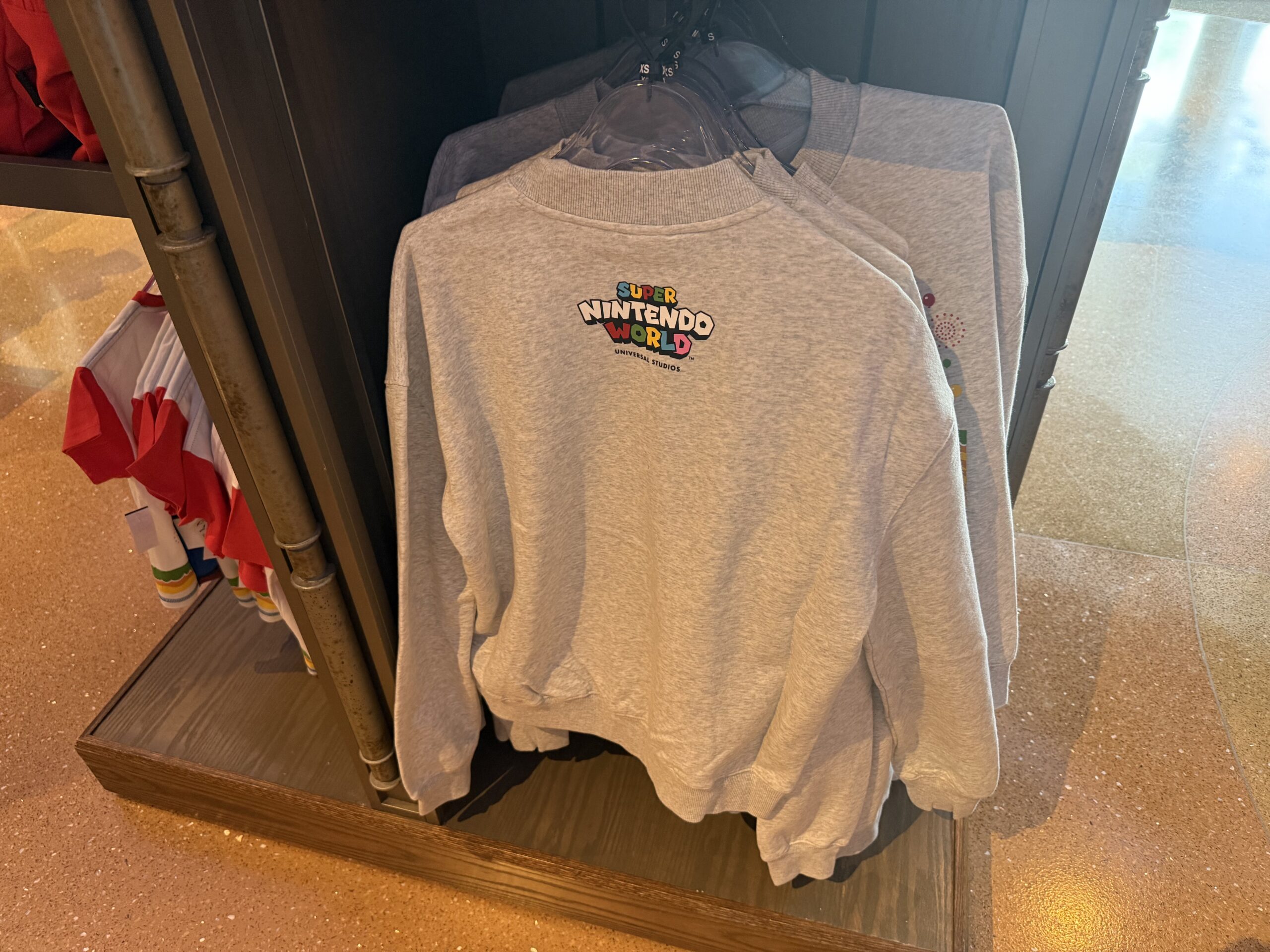 The anniversary design along with the Super Nintendo World are also on the front and back of this light-gray pullover sweatshirt for adults.