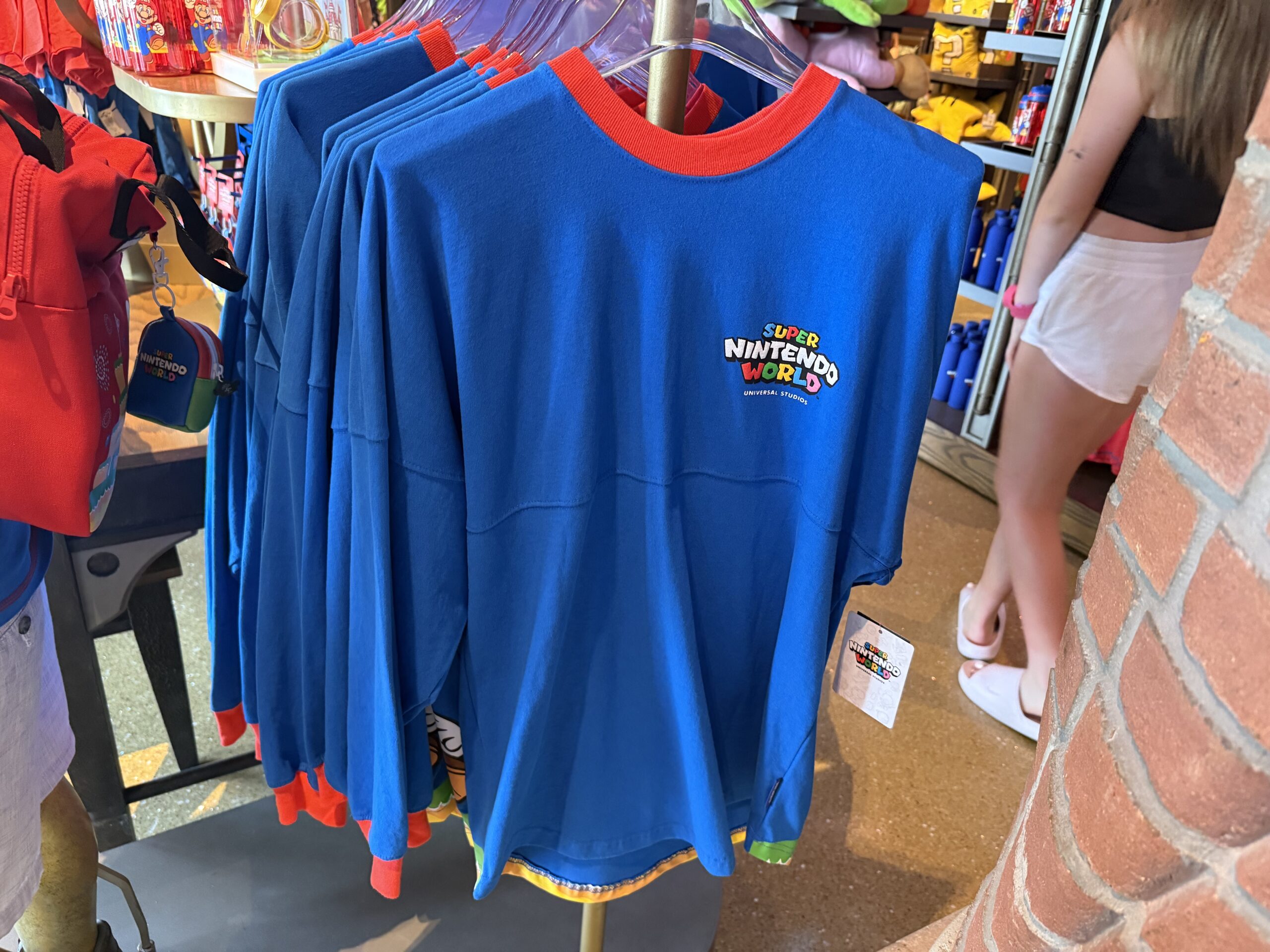 This spirit jersey is blue with a red collar and sleeve cuffs and. The front has the Super Nintendo World logo, while the back has Mario and Mount Beanpole.