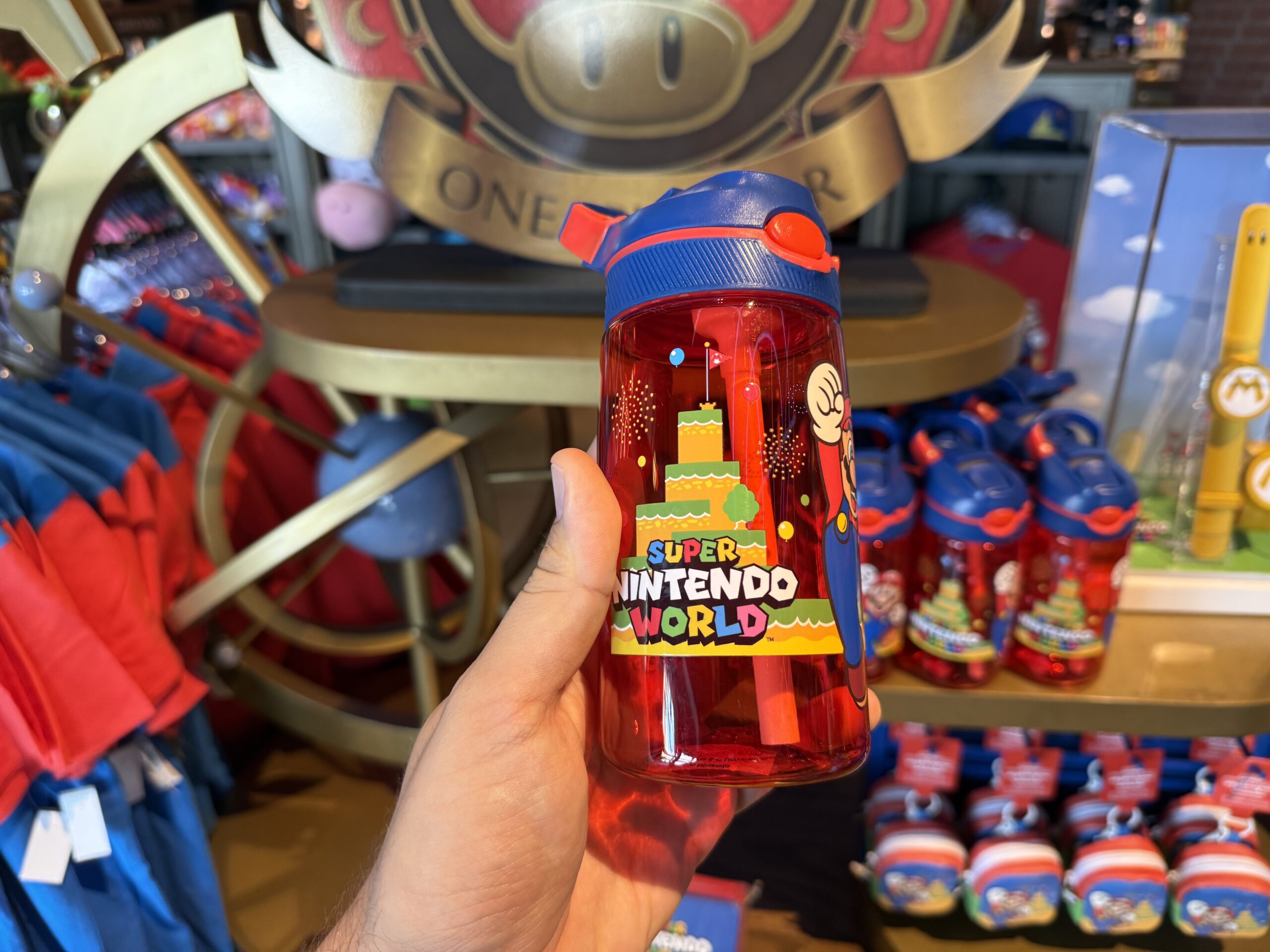This translucent red water bottle has a blue flip-top cap and comes with a straw. Mount Beanpole, Mario, and the Universal Studios logo decorate the sides of the bottle.