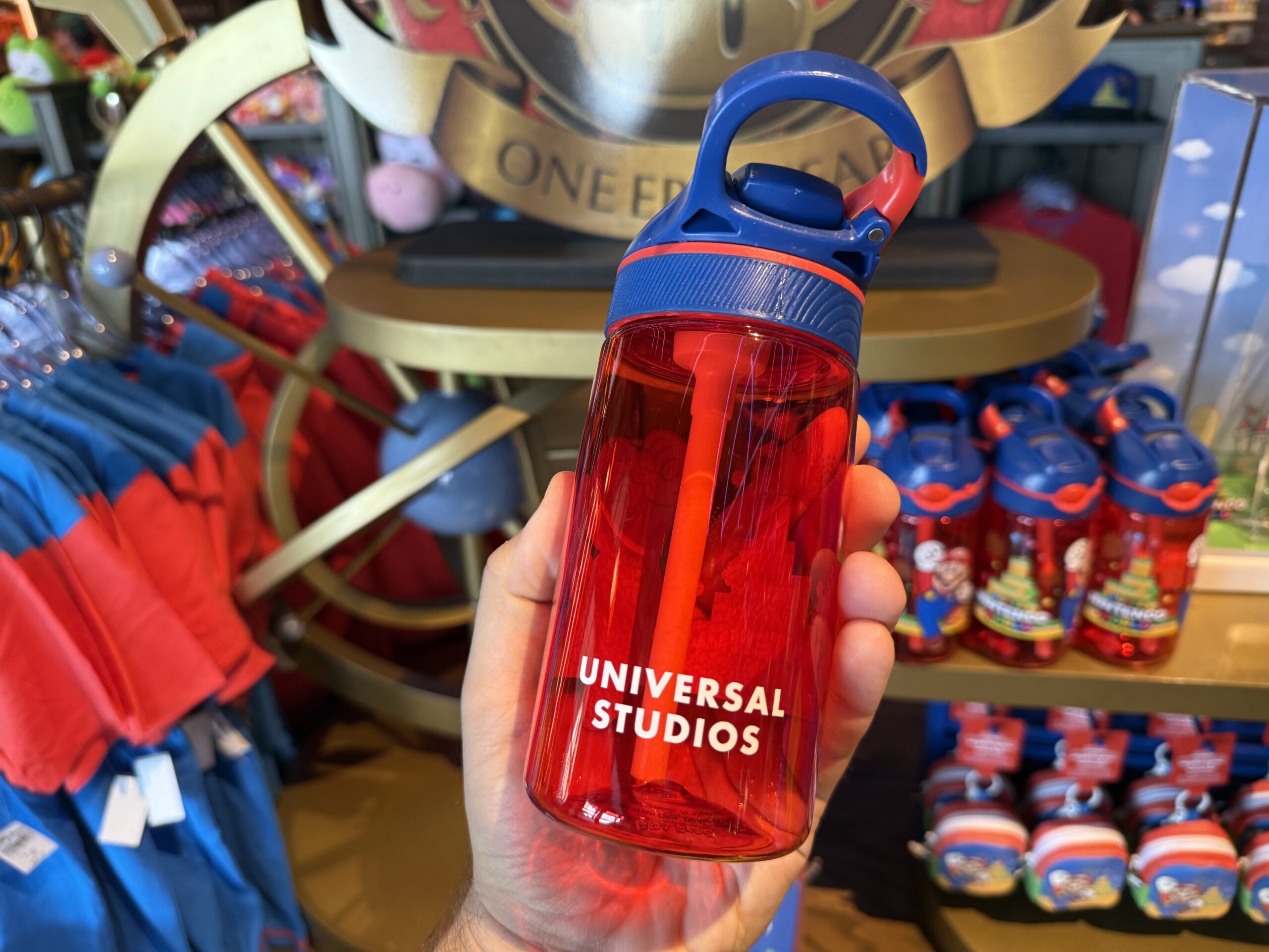 This translucent red water bottle has a blue flip-top cap and comes with a straw. Mount Beanpole, Mario, and the Universal Studios logo decorate the sides of the bottle.