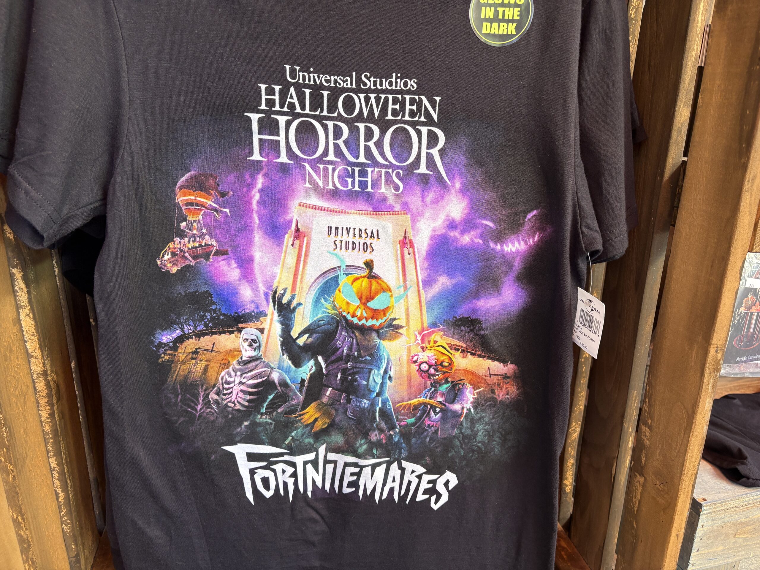 A Skull Trooper, Hollowhead, and Curdle Scream Leader are all pictured in front of the Universal Studios archway. In the purple sky is a tornado and a face with a floating Halloween bus.