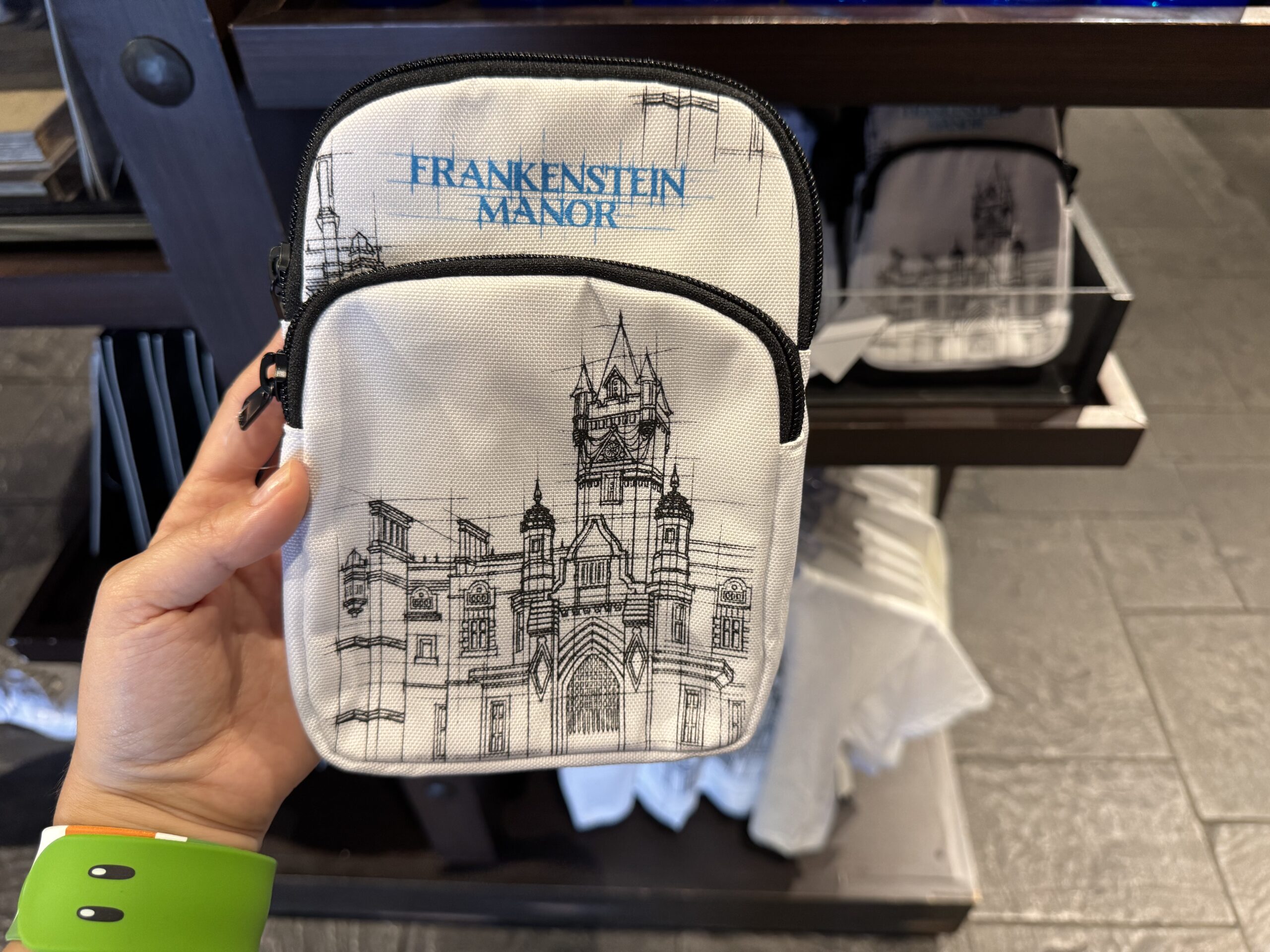 The crossbody is white with a blueprint-style image of Frankenstein Manor. The name of the house is in blue above the art.