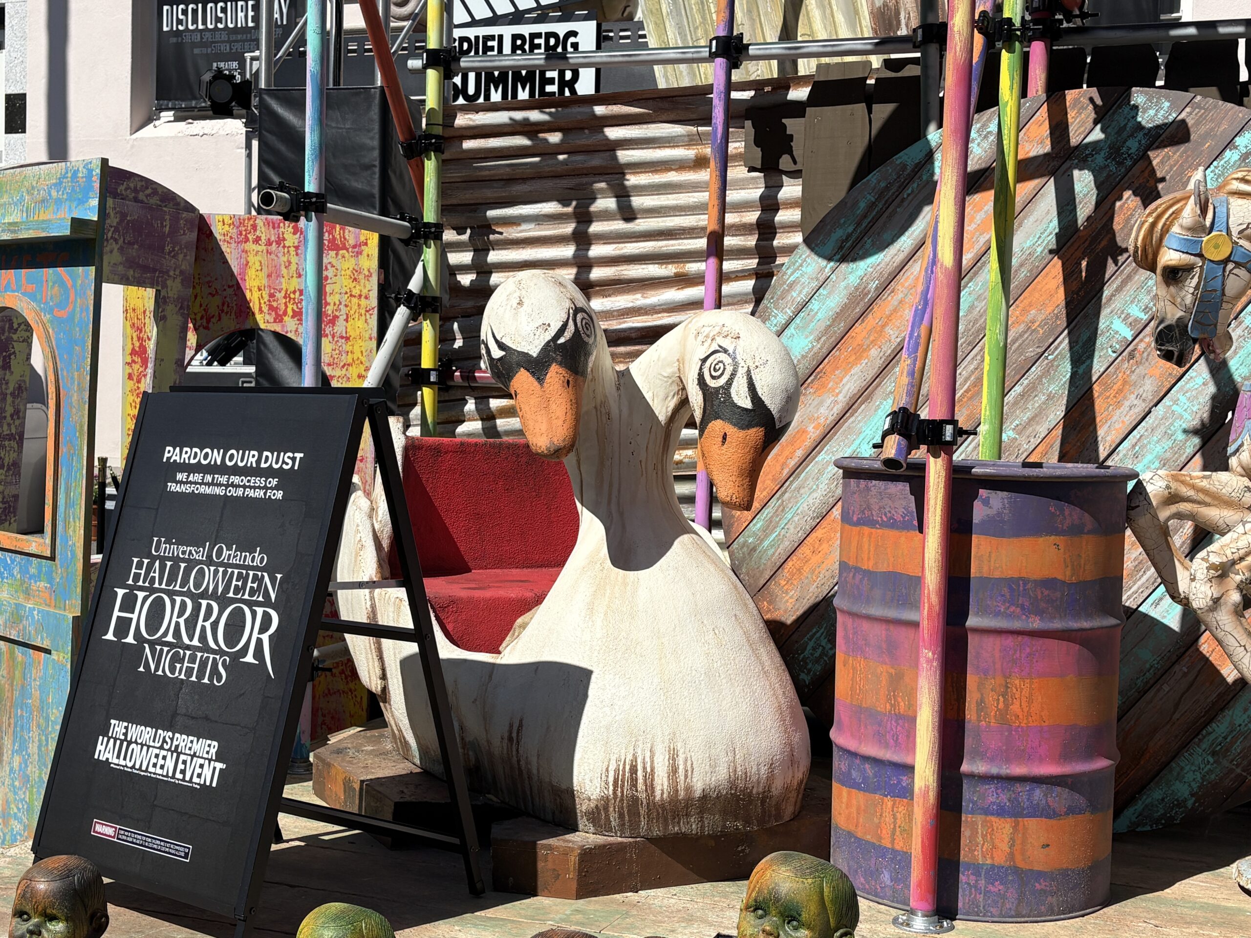 There's a two-headed swan boat — maybe from a Tunnel of Love attraction — and a carousel horse. Around them are colorful barrels and scaffolding.