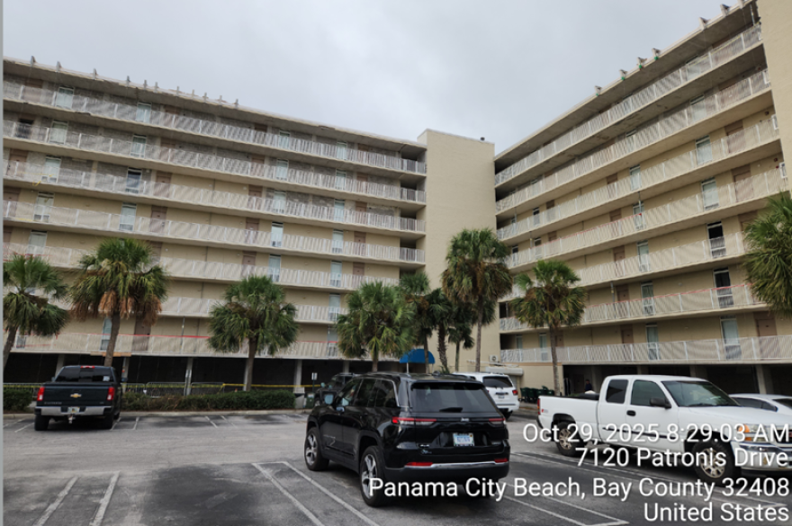 A multi-storied condo building, with yellow-hued walls and cars in the parking lot.