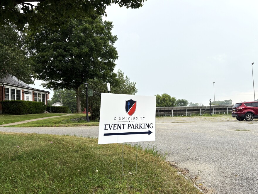 A small sign is staked into the grass next to a parking lot.