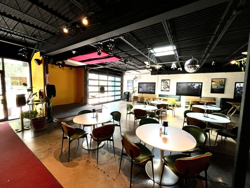 Inside of a nightclub with white round tables facing a stage
