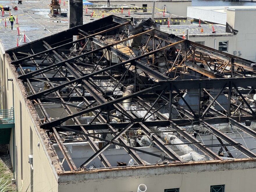 A beige two-story building with the roof only showing charred metal infrastructure and hollow below that.