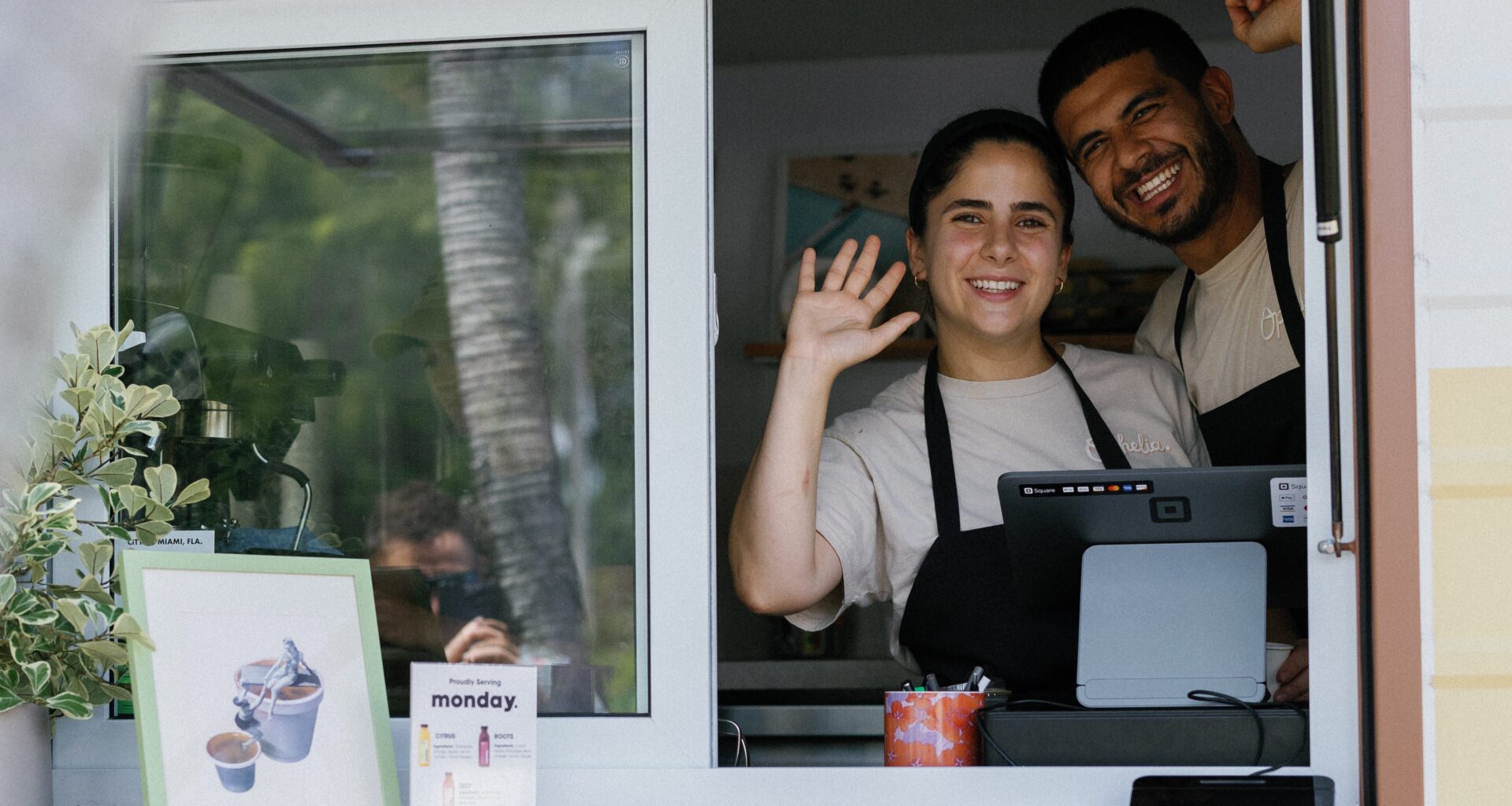 two people wave with glee at a bakery RV window