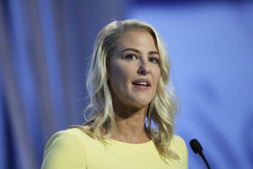 Close-up of Bridget Ziegler looking into the distance behind a microphone, wearing a yellow dress and
