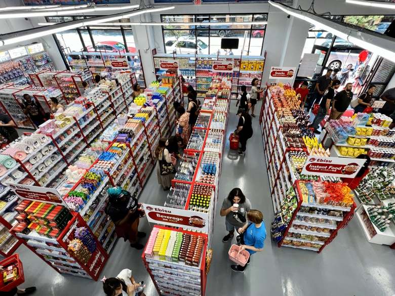 High-angle view of shoppers browsing aisles stocked with Japanese snacks, stationery, and household goods inside an Ebisu store