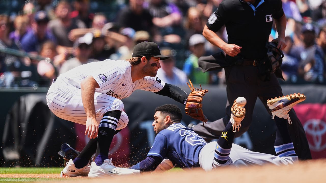 Colorado Rockies third baseman Kyle Karros, front left, fields the throw as Tampa Bay Rays' Victor Mesa Jr. slides safely into third base with a triple while third base umpire Alan Porter waits to make the call in the second inning of a baseball game in Denver, Wednesday, Aug. 5, 2026. (AP Photo/David Zalubowski)