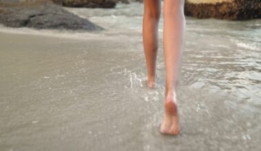 Person walking barefoot through shallow seawater along a sandy beach.