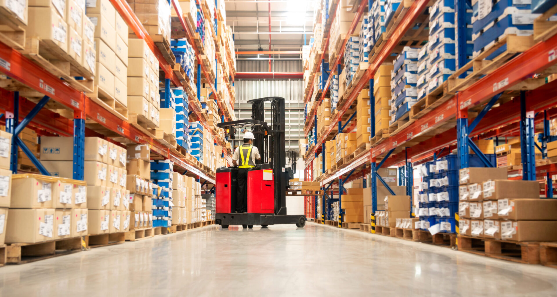Warehouse worker operating a forklift between rows of pallet racks filled with boxes