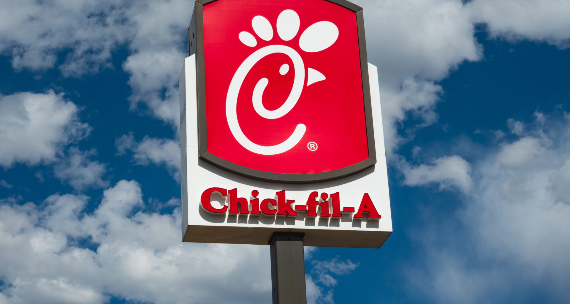Chick-fil-A sign against a blue sky with clouds
