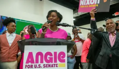Angie Nixon speaks at podium surrounded by supporters