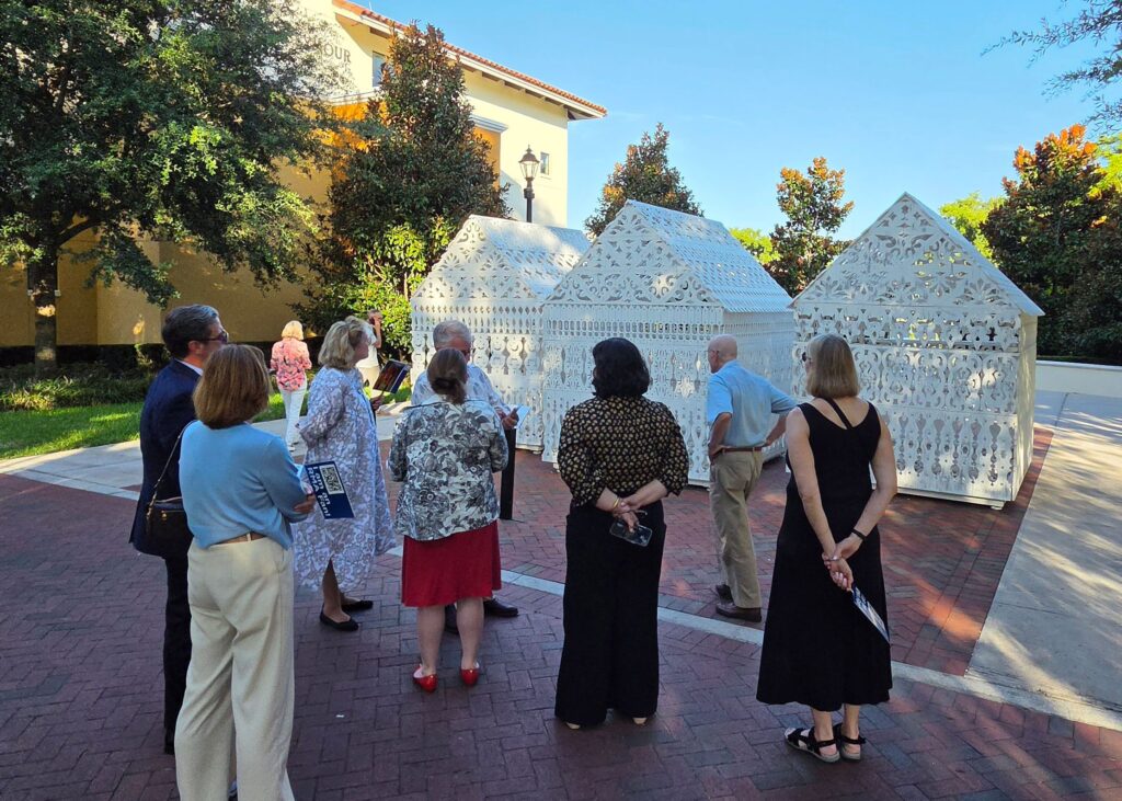 People looking at three white structures that are part of an art installation.