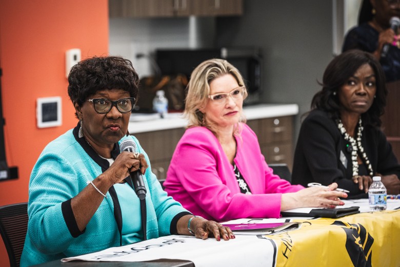 A photograph by Dave Decker showing Hillsborough County Commissioner Gwen Myers on the left and Aileen Rodriguez in the center seated at a panel table at the C. Blythe Andrews Jr. Public Library in Tampa, Florida, on July 9, 2026. Captured in a wide shot, Myers speaks into a microphone while wearing a turquoise cardigan with black trim and dark-rimmed glasses. Seated next to her, Rodriguez wears a bright magenta pink blazer and cat-eye glasses, listening intently alongside a third panelist seated on the right in a dark jacket.