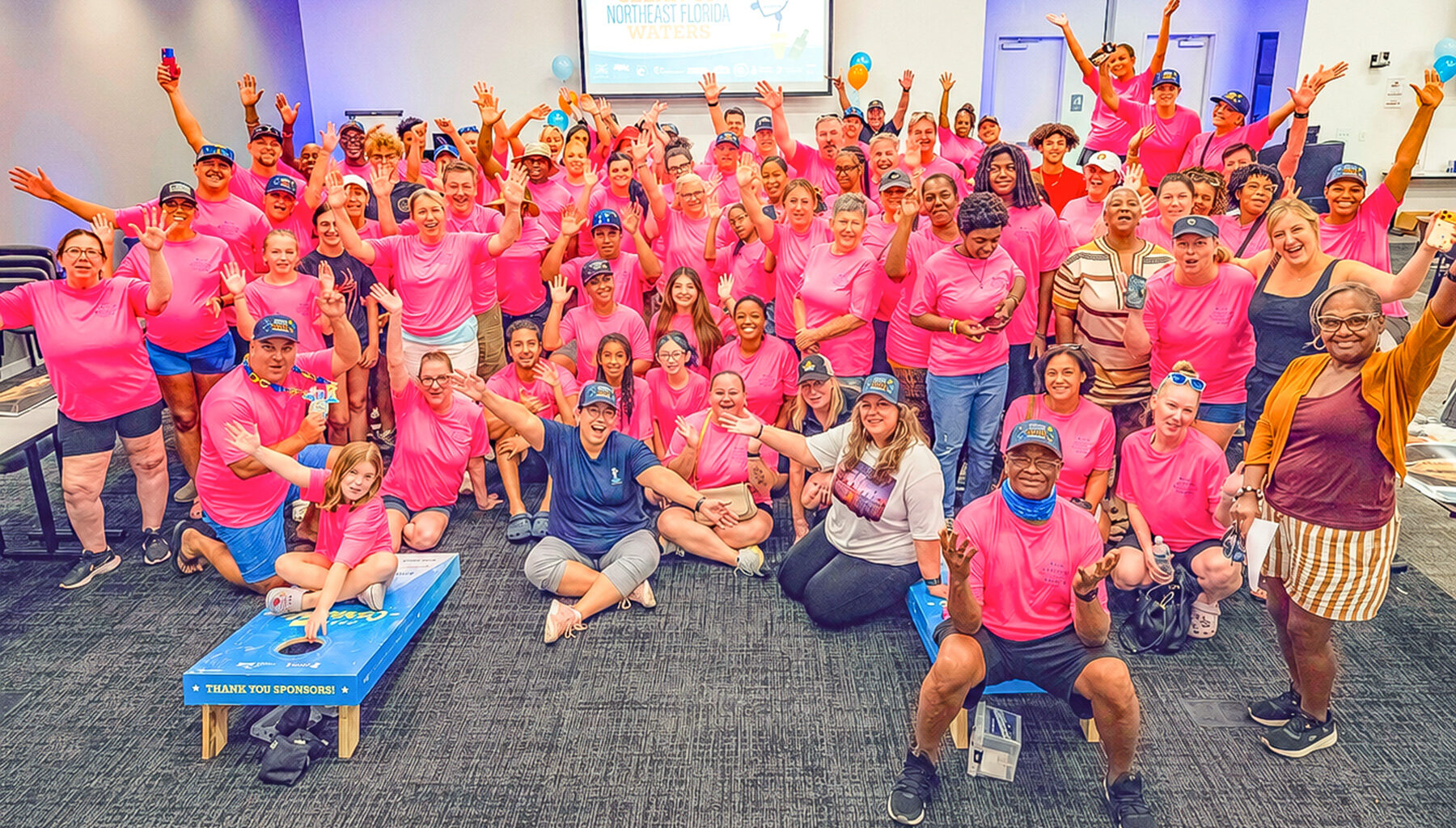 large group of NEFAR volunteers in pink shirts with their hands up and smiling