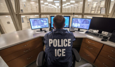 A photo of an ICE officer monitoring live video feed of a detention facility.