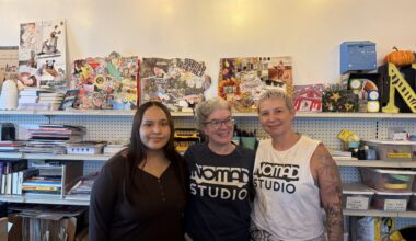 Misha (left), Carrie Boucher (Center), Kinsey Rodriguez (left) in front of collages and artwork in the St Pete office of NOMADstudio. August 11, 2026. Photo by Juanita Hurtado Huerfano/ WMNF news.