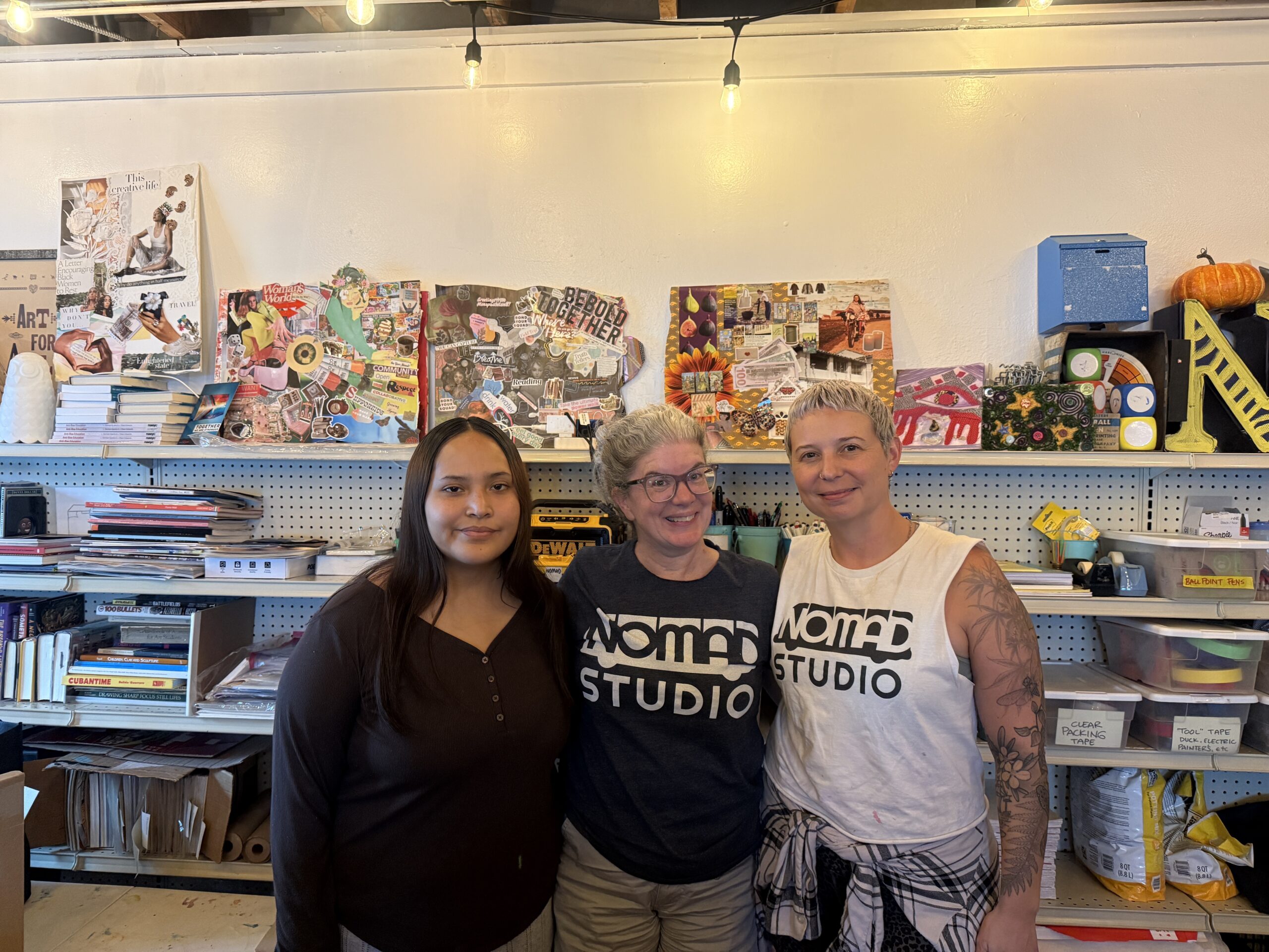Misha (left), Carrie Boucher (Center), Kinsey Rodriguez (left) in front of collages and artwork in the St Pete office of NOMADstudio. August 11, 2026. Photo by Juanita Hurtado Huerfano/ WMNF news.